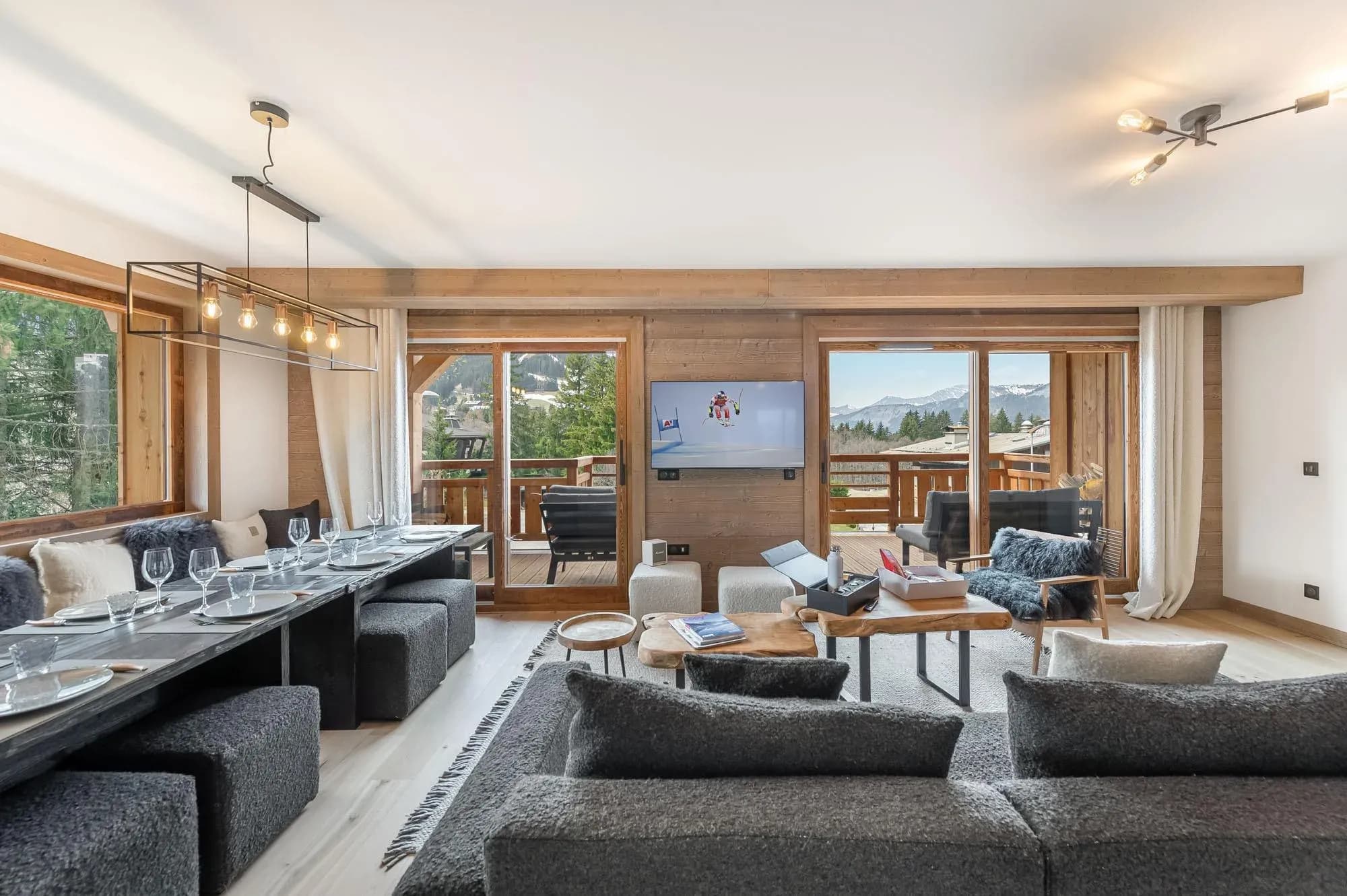 Living area with grey sofa, long dining table and balcony doors to mountain views