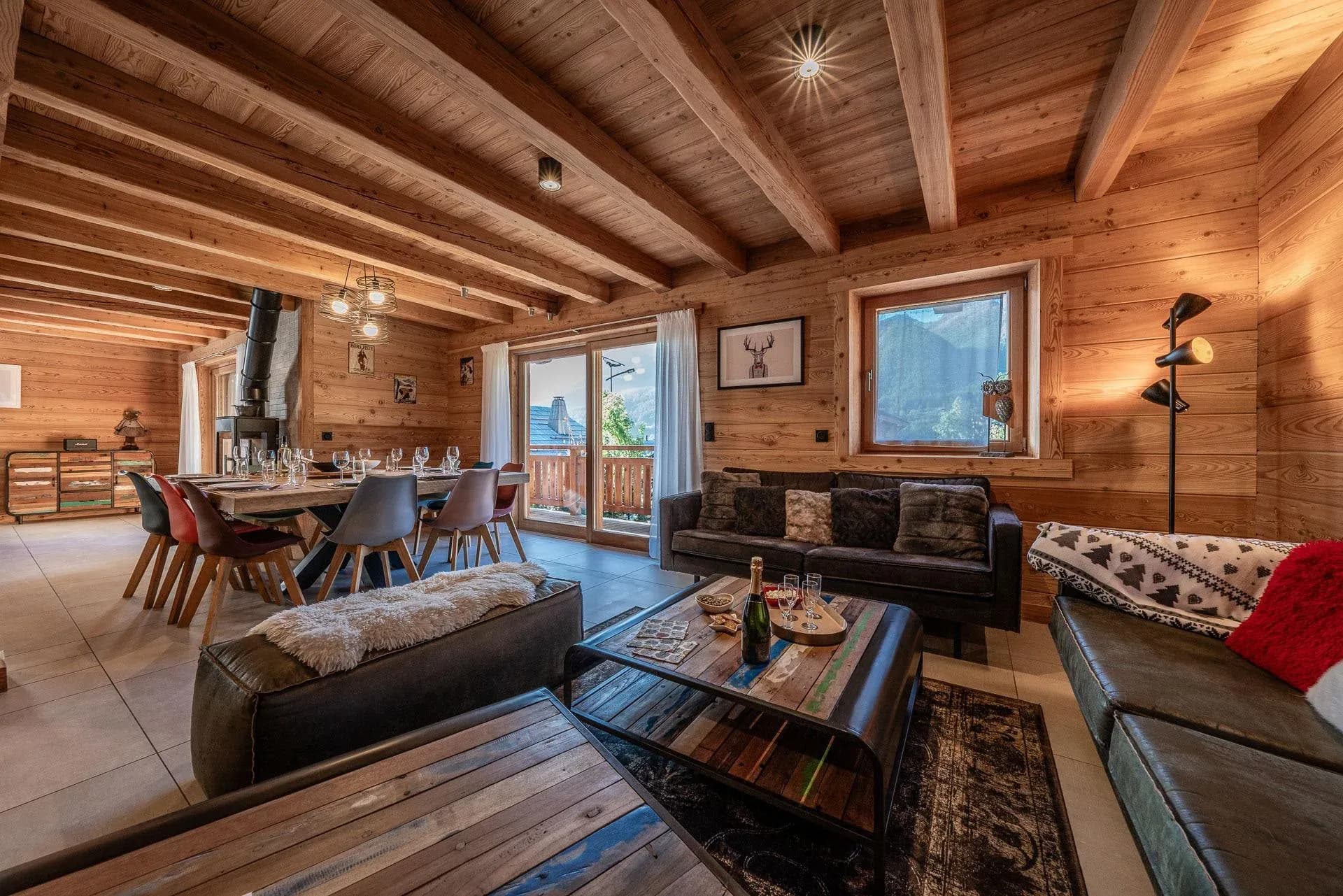 Lounge with leather sofas, reclaimed-wood coffee table and dining table behind, balcony doors to the mountains