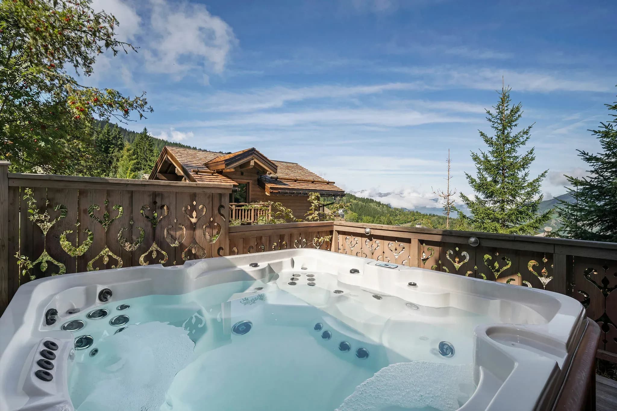 Outdoor hot tub on terrace with carved wooden screen and mountain view