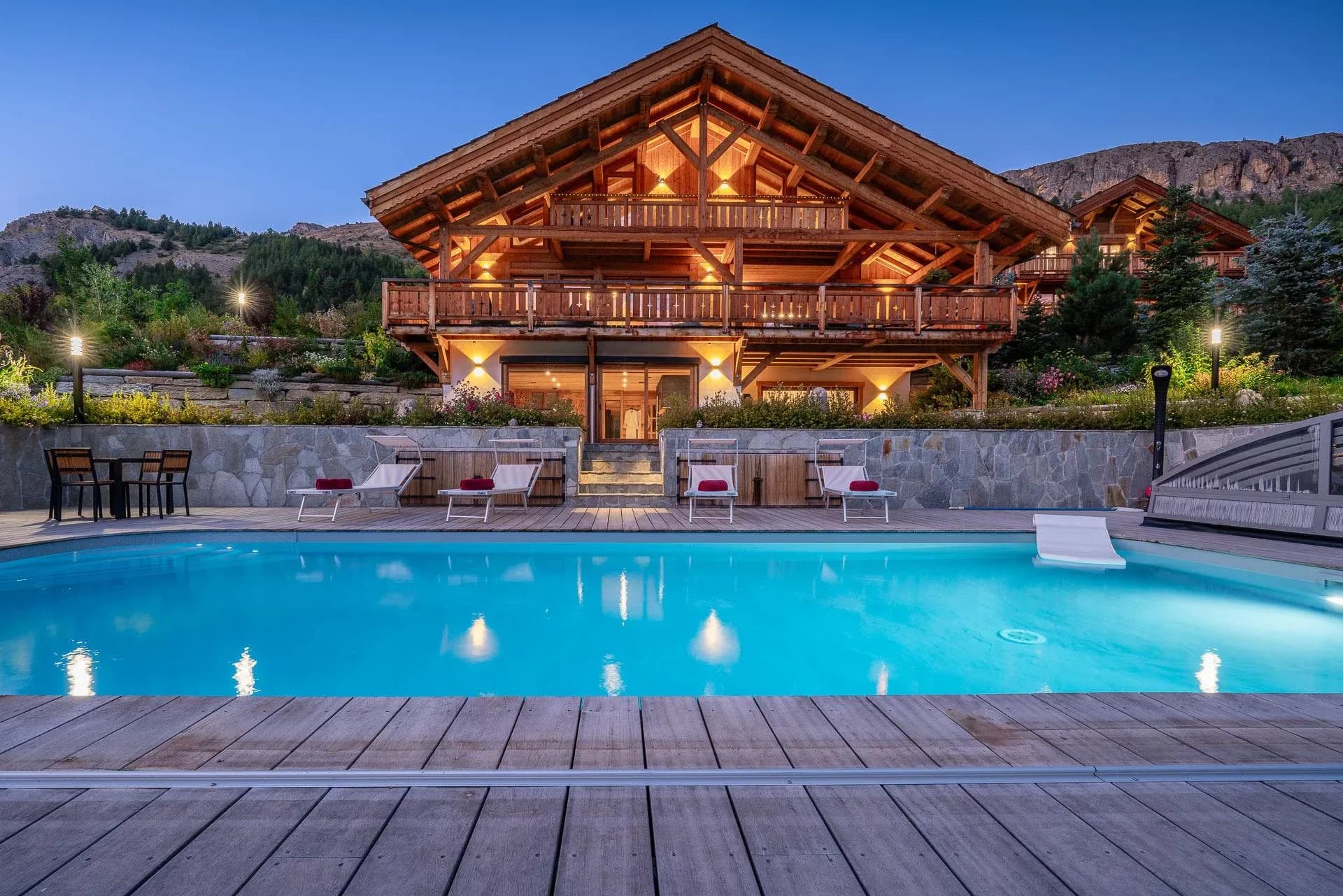 Chalet at dusk with outdoor pool, sun loungers and wooden balconies