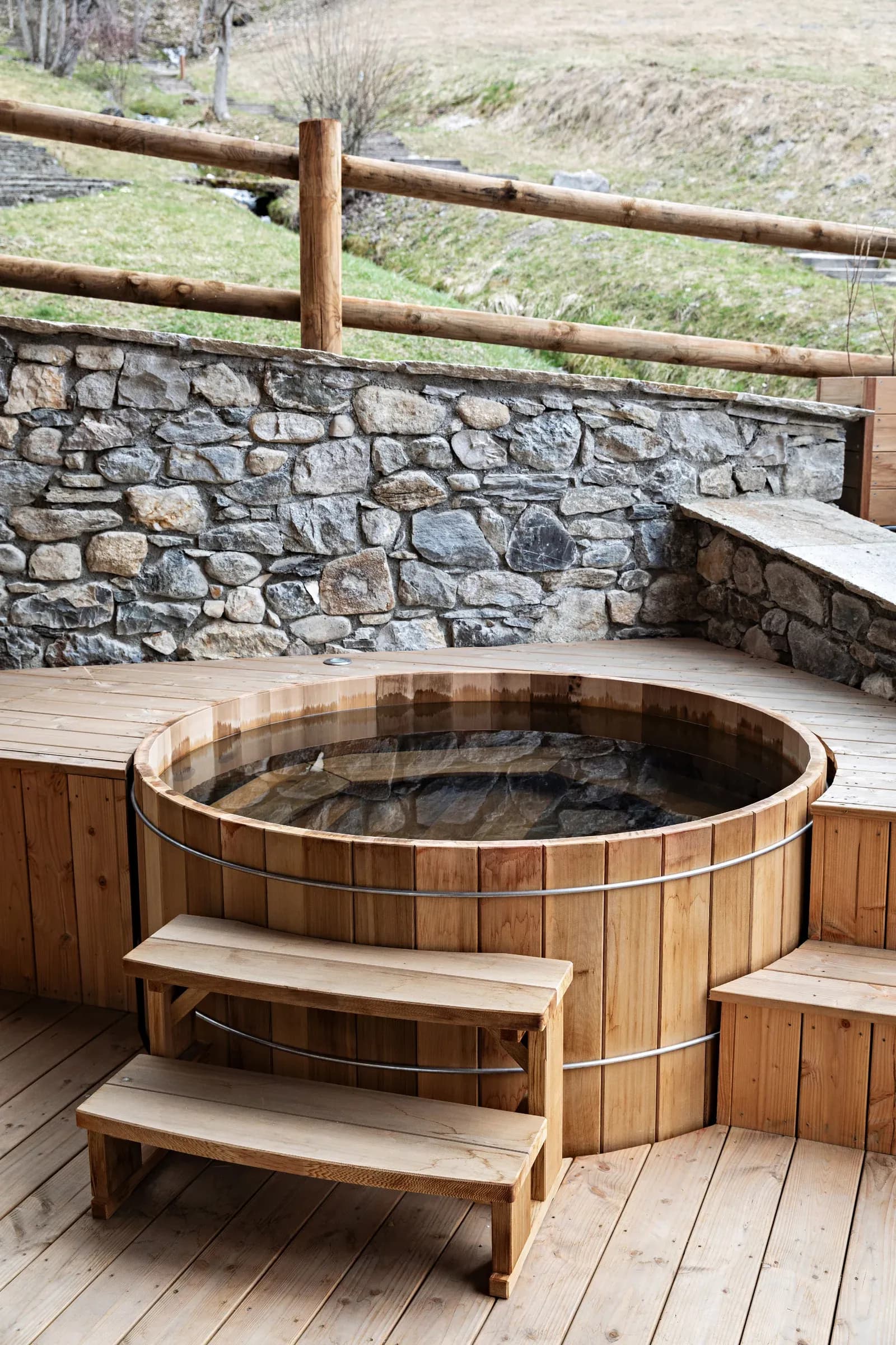 Wooden hot tub on a deck with steps and stone wall