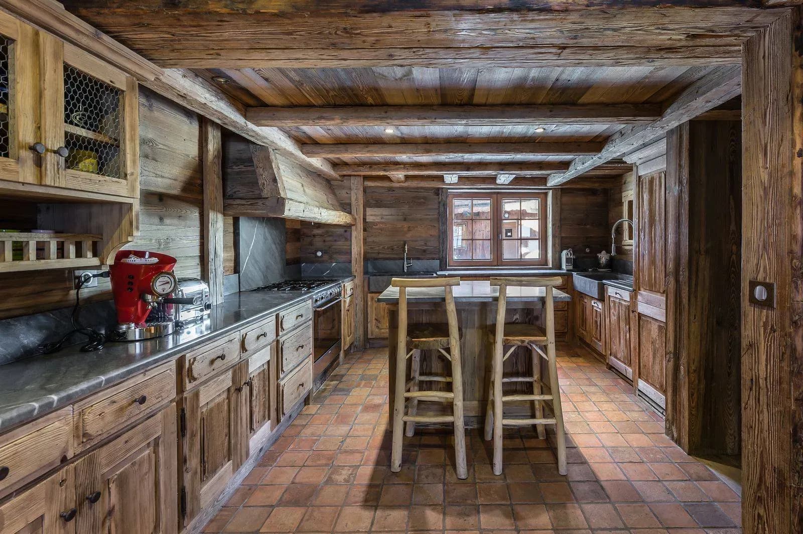 Kitchen with zinc worktops, gas range, terracotta floor and two wooden bar stools at the island
