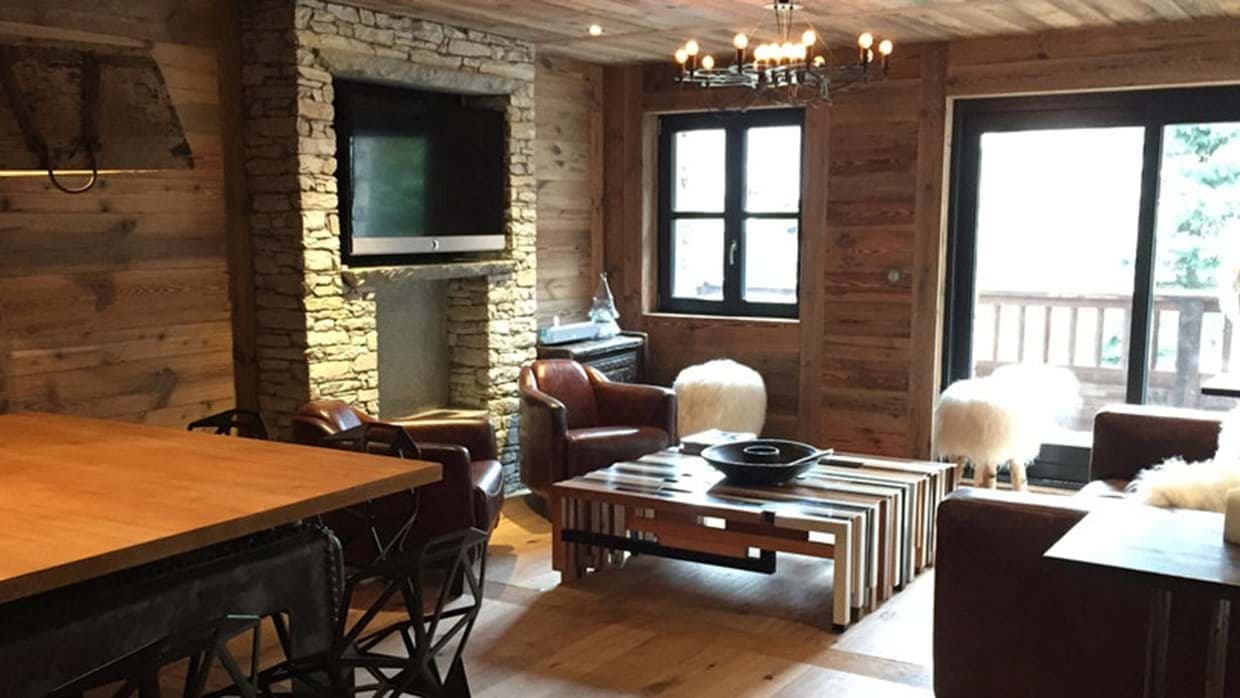 Living area with wood-clad walls, stone fireplace, and balcony access
