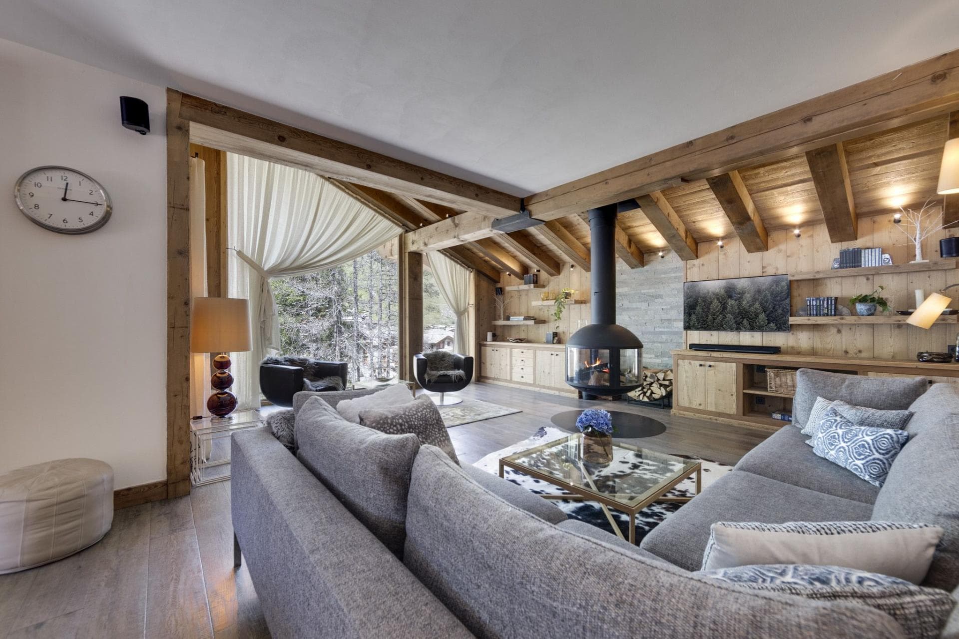 Living area with wood-burning pivot fireplace and floor-to-ceiling forest views