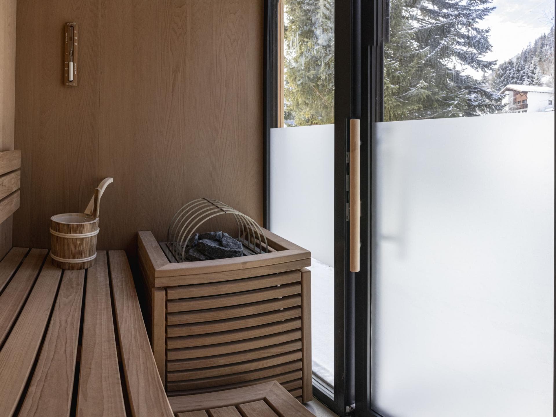 Private sauna with wood-fired heater and snowy forest views through floor-to-ceiling windows
